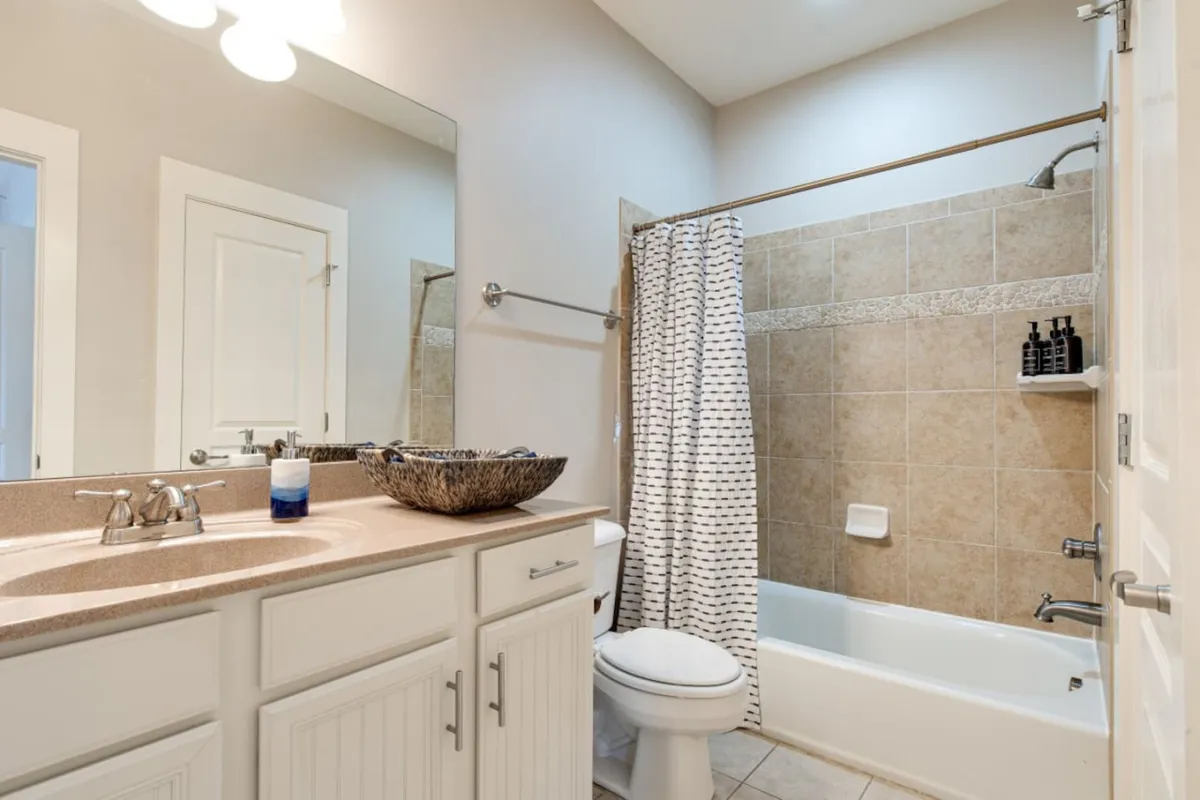 A serene and modern en-suite bathroom featuring a sink with basin, bathtub, shower area, large mirror, and towel rack. The space is inviting and well-equipped for personal grooming and relaxation.