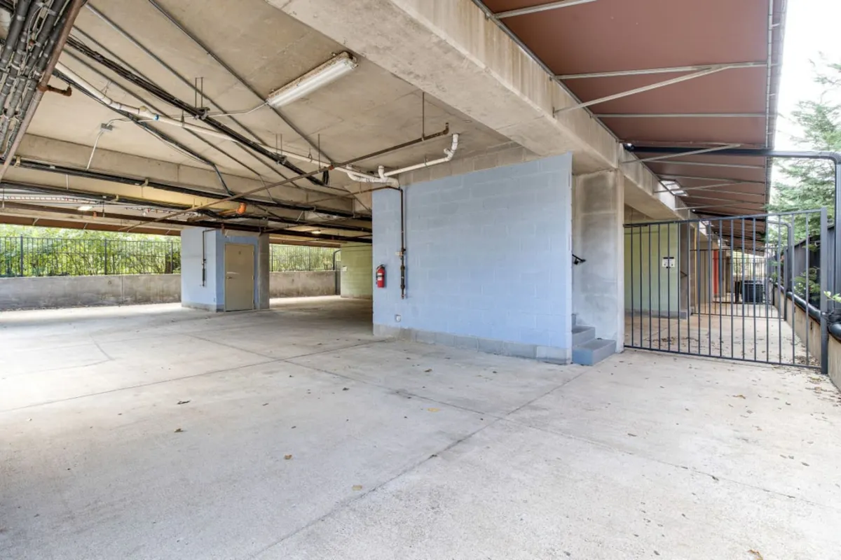 An exterior view highlighting the concrete parking surface, security gate, and accessible entry, designed for vehicle parking and secure access. The gated environment reinforces the sense of safety and organization for both residents and their guests.