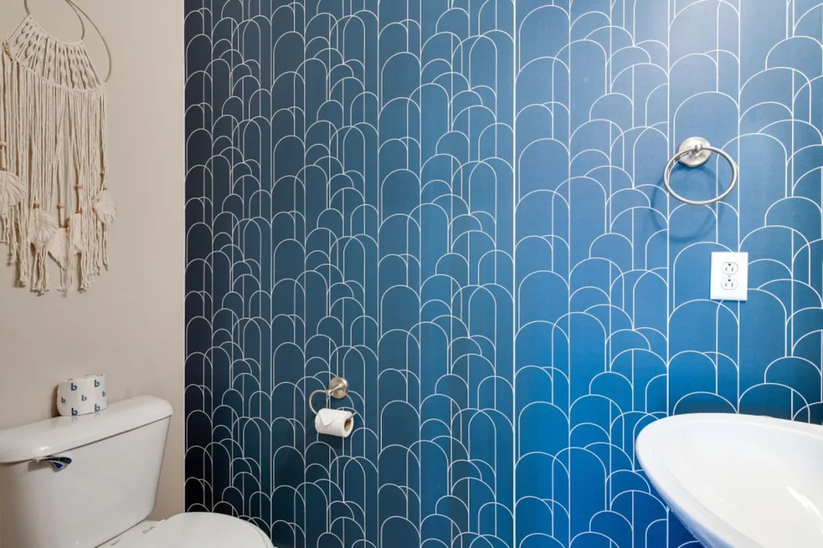 A chic half bath with a striking blue patterned wall, toilet, and decorative macrame, creating a serene atmosphere for guests and residents alike.